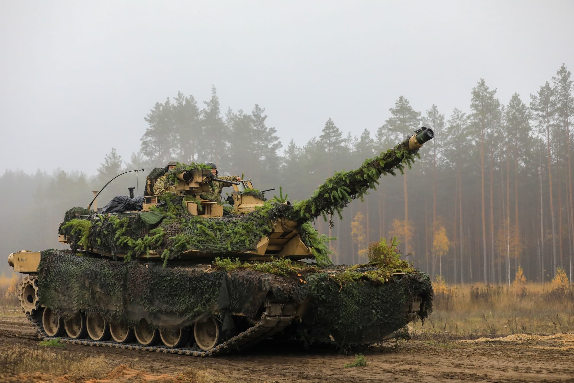 Camouflaged U.S. Army M1A2 Abrams tank moves across a dirt training ground