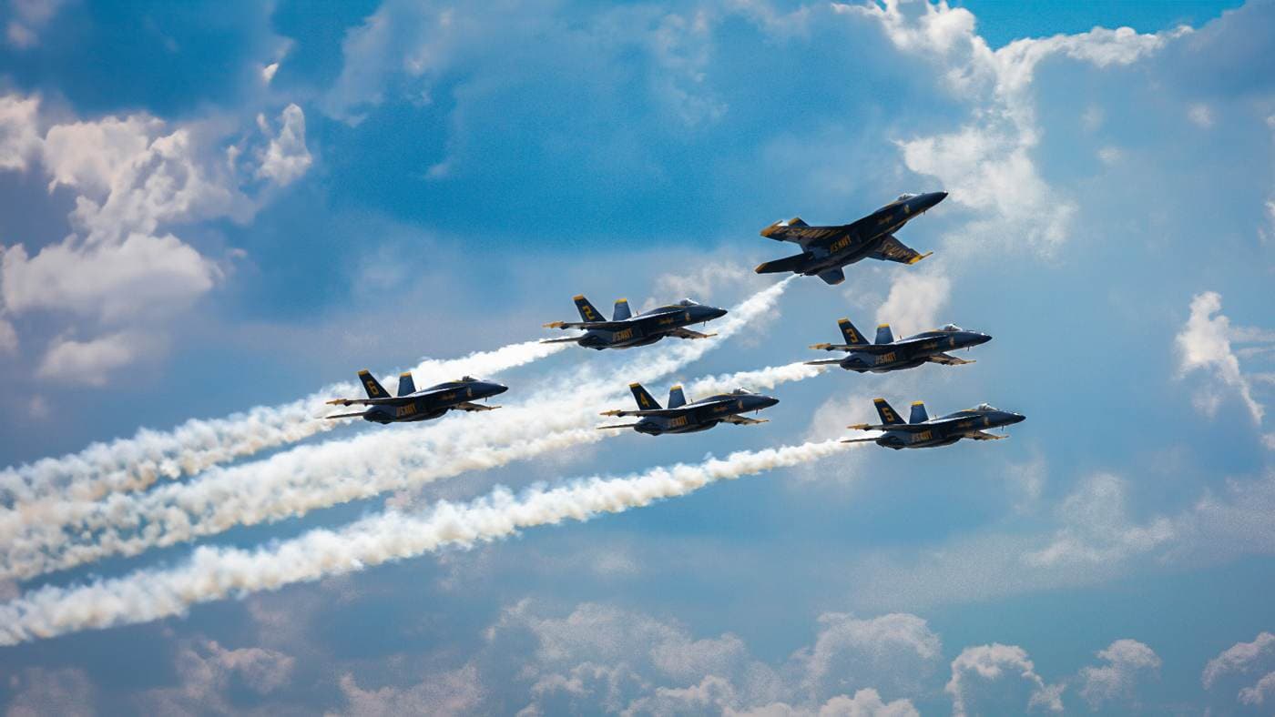U.S. Navy Blue Angels aircraft flying in formation with vapor trails across a blue sky